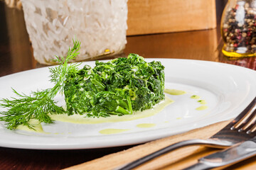 Wall Mural - Cooked spinach with garlic on a white plate. Vegetarian food.