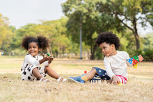 Cheerful Two African American Little Boy And Girl Playing Toy Together In The Park. Children With Curly Hair Having Fun Together Outdoor. Black Kid People Enjoying Outside