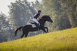 portrait of rider man and black stallion horse during eventing cross country competition in summer