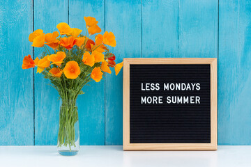 Wall Mural - Less mondays more summer. Motivational quote on letter board and bouquet orange flowers on white table against blue wooden wall. Concept inspirational quote of the day. Front view