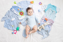 A Baby In Blue Clothes Is Lying Among Children's Accessories And Clothes
