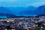 Fototapeta Uliczki - Aerial panorama of beautiful Lucerne City by lakeside at blue dusk with majestic mountains in background and lights of houses under evening twilight before nightfall, in Switzerland, Europe
