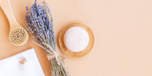 Flatlay Composition With Lavender Flowers And Natural Cosmetic Products. Organic SPA Cosmetic. Massaging Face Brush, Soap Bar, Sea Salt And Bamboo Towel On A Beige Background. Banner