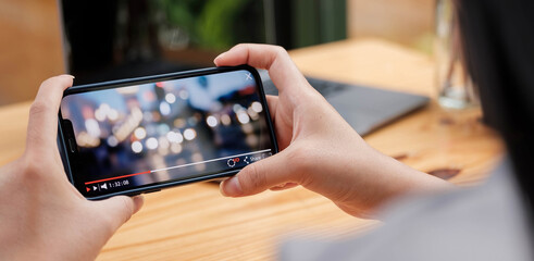 Cropped image of female hand holding smartphone and watching video while standing outdoor.