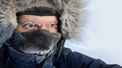 traveler in the arctic. portrait of a freezing man in winter clothes, a hood and a warm mask. ice on