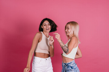 Wall Mural - Two girl friends in casual on pink background having fun together, smile and laugh, friendship concept
