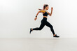 Side view of woman running against a white wall. Jogger with kinesiology tape on her shoulder sprinting.