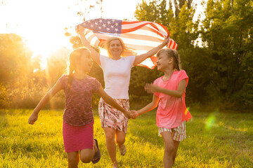 Wall Mural - parents and child with American flag are playing with a colorful kite. mother, father and their little daughters celebrate together 4th of July outdoors in foggy day. Independence Day of USA concept.