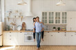 © fizkes - Portrait of affectionate young wife sitting on kitchen counter hug smiling husband from behind at modern renovated interior. Loving young couple homeowners look at camera glad of buying new furniture