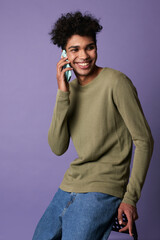 Wall Mural - Portrait of young brunette man sitting mobile in hand on purple background