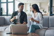 © gstockstudio - Beautiful young couple drinking coffee and looking on the laptop while sitting on the sofa at home
