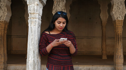 Wall Mural - Young Indian female using a smartphone leaning on a column