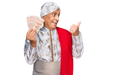 Poster - Senior hispanic man wearing sherwani costume holding 50 indian rupee banknotes pointing thumb up to the side smiling happy with open mouth