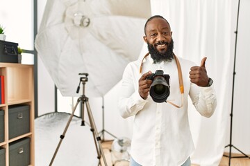 African american photographer man working at photography studio doing happy thumbs up gesture with hand. approving expression looking at the camera showing success.