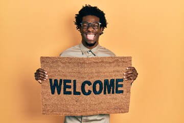 Sticker - Young african american man holding welcome doormat sticking tongue out happy with funny expression.