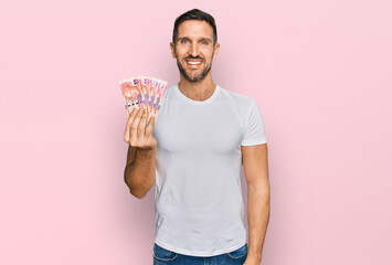 Wall Mural - Handsome man with beard holding south african 50 rand banknotes looking positive and happy standing and smiling with a confident smile showing teeth