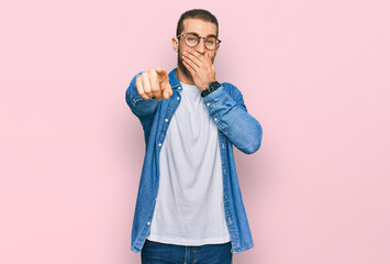 Poster - Young caucasian man wearing casual clothes laughing at you, pointing finger to the camera with hand over mouth, shame expression