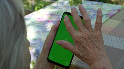 a smartphone in the hand of an old woman in her garden, who is looking at the pages, a green screen