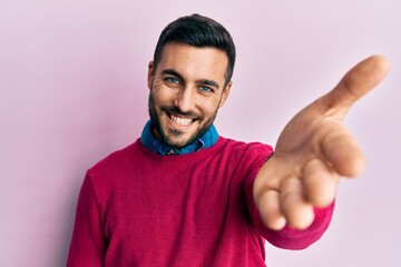 Sticker - Young hispanic man wearing casual clothes smiling cheerful offering palm hand giving assistance and acceptance.