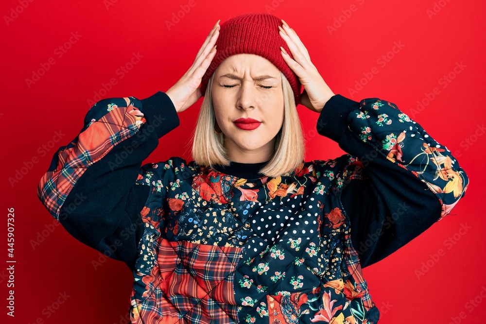 Young blonde woman wearing wool winter cap suffering from headache desperate and stressed because pain and migraine. hands on head.