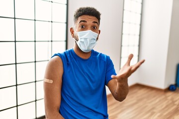 Wall Mural - Young hispanic man with beard wearing safety mask getting vaccine celebrating victory with happy smile and winner expression with raised hands