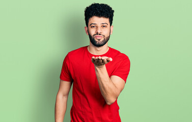 Poster - Young arab man with beard wearing casual red t shirt looking at the camera blowing a kiss with hand on air being lovely and sexy. love expression.