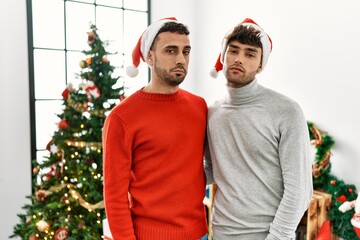 Poster - Young gay couple standing by christmas tree wearing hat looking sleepy and tired, exhausted for fatigue and hangover, lazy eyes in the morning.