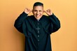 © Krakenimages.com - Young latin priest man standing over yellow background smiling pulling ears with fingers, funny gesture. audition problem