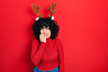 Sticker - Young middle east woman wearing cute christmas reindeer horns looking stressed and nervous with hands on mouth biting nails. anxiety problem.