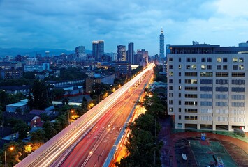 Wall Mural - Night scape of a busy street at rush hour in Downtown Taipei, the capital city of Taiwan, with traffic trails on an elevated expressway between high-rise buildings & Taipei 101 Tower in blue twilight