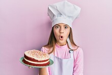 Beautiful Brunette Little Girl Wearing Baker Uniform Holding Homemade Cake Scared And Amazed With Open Mouth For Surprise, Disbelief Face