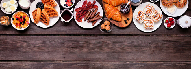 Poster - Breakfast or brunch top border on a dark wood banner background. Above view. Assortment of sweet and savory food items.