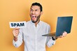 © Krakenimages.com - Hispanic man with beard working using computer laptop holding spam banner angry and mad screaming frustrated and furious, shouting with anger. rage and aggressive concept.