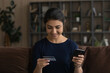 © fizkes - Happy millennial Indian woman hold cellphone shopping online with credit debit card at home. Smiling young mixed race female buyer client make payment buy on web use smartphone. Consumerism concept.