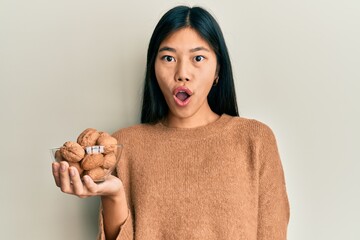 Sticker - Young chinese woman holding bowl with walnuts scared and amazed with open mouth for surprise, disbelief face