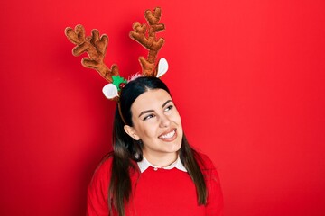 Canvas Print - Young hispanic woman wearing cute christmas reindeer horns looking away to side with smile on face, natural expression. laughing confident.