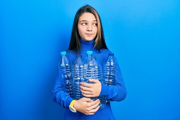 Poster - Young brunette girl holding recycling plastic bottles smiling looking to the side and staring away thinking.