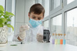 © Anna - Boy in protective medical robe, mask and gloved holds pipette and glasses and prepare to look into little microscope. Scientifil experiments of young scientist.