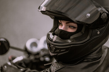 Stylish motorcyclist woman in helmet and leather jacket sitting on black motorcycle. Female driver outdoors on nature background. Trip, cafe racers, speed, freedom concept.