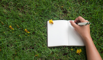 female hands with pen writing on notebook on grass outside