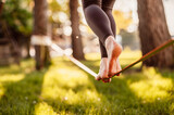 Fototapeta  - Slacklining is a practice in balance that typically uses nylon or polyester webbing. Girl walking on a slackline in a park during a sunset. Slack line