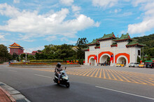 A Motor Scooter Moving Fast On The Road By The Entrance Gate To Martyr Shrine In Dazhi, Taipei, Taiwan And Majestic Grand Hotel, A Famous Landmark Building Of Traditional Chinese Style, In Background