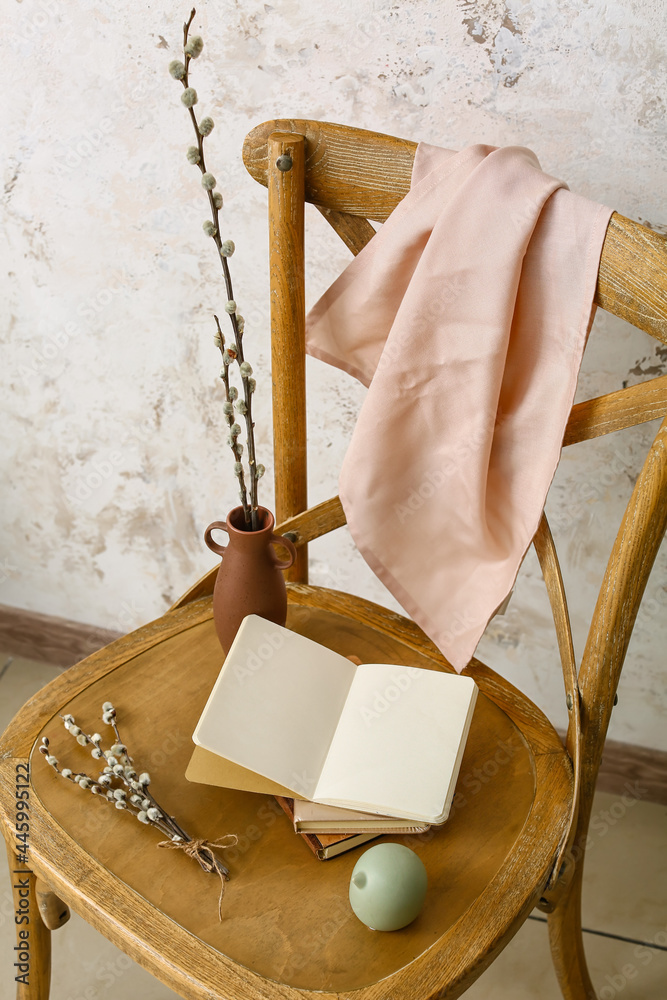 Chair with willow branches and books near light wall