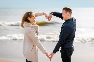 Happy young couple making heart shape with arms on sea beach against spring,autumn evening.