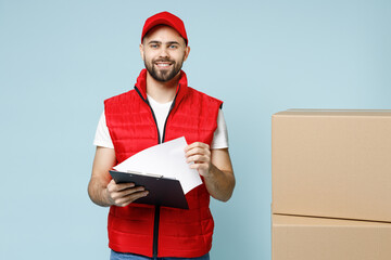 Wall Mural - Professional delivery guy employee man in red cap white T-shirt vest uniform workwear work as dealer courier hold blank cardboard box isolated on pastel blue color background studio. Service concept.