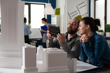 Poster - Design architecture colleagues sitting at office working on tablet and blueprints for layout plan maquette building model. Professional engineering team sitting for construction project