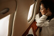 Businesswoman brunette with glasses in a white jacket flies in a charter business jet looks out the window and smiles, she is happy with his departure