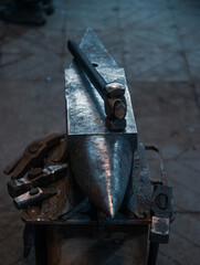 Various blacksmith tools around the anvil with a hammer. Dark toning.