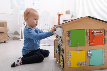 Wall Mural - Cute little boy playing with busy board house on floor at home