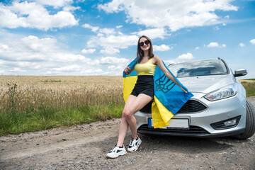 happy beautiful young woman with flag of ukraine standing near her car